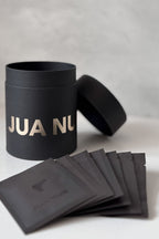 Black cylindrical container with 'JUA NUR' branding, accompanied by black packets on a light gray background.